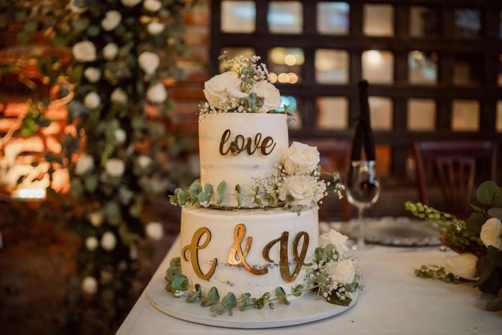 Bolo de casamento semi-naked texturizado com iniciais douradas e flores como alternativa aos bonecos de bolo personalizados.