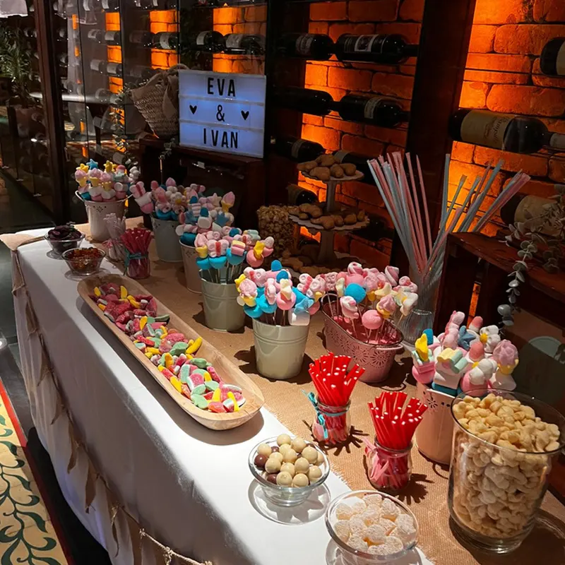 Letras luminosas de madeira pequenas com a palavra BAR acesas sobre uma mesa de doces e cocktails de casamento.