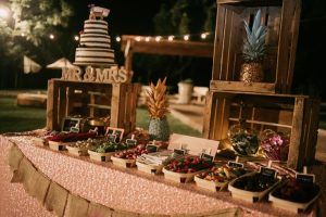 Letras decorativas brancas recortadas com os nomes dos noivos dispostas numa mesa de doces com queques e suportes de vidro.