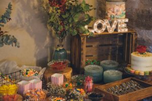 Mesa de doces casamento decorada com letras gigantes luminosas com a palavra LOVE e pastelaria fina num espaço rústico.