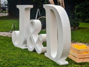 Duas letras gigantes tridimensionais brancas J e D, com um ampersand pequeno, sobre o relvado de uma quinta.