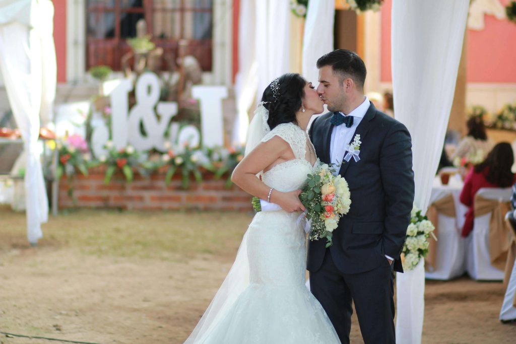 Noivos a posar num casamento ao ar livre com letras XXL personalizadas em esferovite ao fundo, criando um cenário fotográfico perfeito.