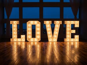 Letras XXL iluminadas com lâmpadas formando a palavra LOVE num cenário para festas à noite.