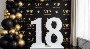Número 18 gigante de esferovite branco com acabamento liso ao lado de um painel VIP preto e dourado com balões numa festa de aniversário.