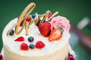Topo de bolo de casamento moderno com a palavra love em madeira e decoração de frutos vermelhos.